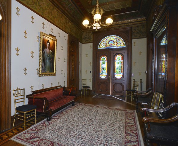 Magnificent double doors with stained-glass panels open into the large entry hall which was intended to impress with its gold leaf fleur-de-lis patterned walls, expensive oriental carpet, and family portrait of “Miss Daisy.”
