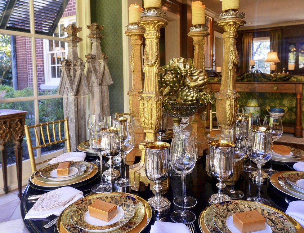 Another angle of the sunroom with its gold-themed place settings, artichoke and holly centerpiece, and tall candlesticks.