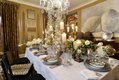 The dining room table is a glistening holiday wonderland with sterling flatware, silvery ruffled china, sparkling crystal, towering white table-top trees, copious candles, and extravagant flowers.