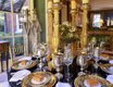 Another angle of the sunroom with its gold-themed place settings, artichoke and holly centerpiece, and tall candlesticks.
