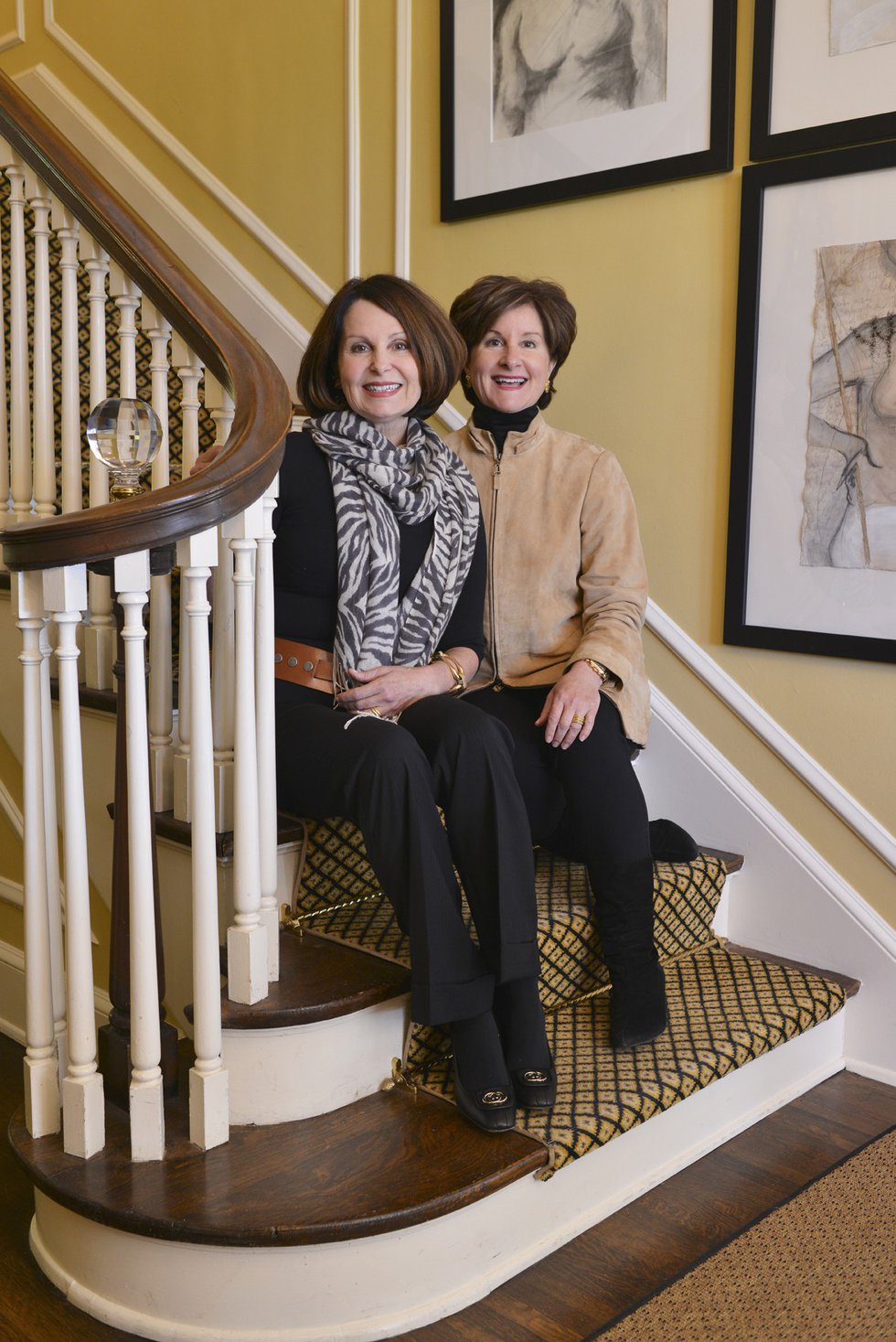 Sisters and business partners Ruthie and Russell pose on the stairs beneath artwork by Bliss Campbell, Ruthie’s daughter, who lives in New York City. 
